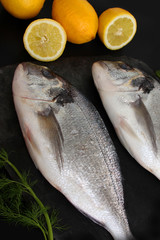 two pieces fresh raw atlantic sea fish with vegetables lie on a black stone board, the concept of cooking seefood