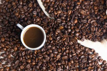 Coffee beans in a rustic coffee bag, full cups and hand holding the coffee