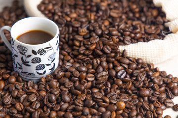 Coffee beans in a rustic coffee bag, full cups and hand holding the coffee
