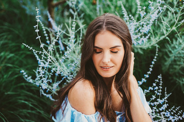 Outdoor close up portrait of pretty young woman with dark hair posing in summer garden with purple...