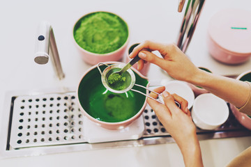 View from the top closeup photo of a green matcha tea making process. Woman's hands holding a...