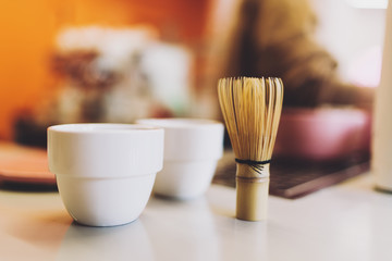 A set of two cups for the green matcha tea and a traditional bamboo whisk for whipping matcha powder. Tea making ceremony in an asian coffee shop. Healthy and tasty beverage. Vegetarian lifestyle.