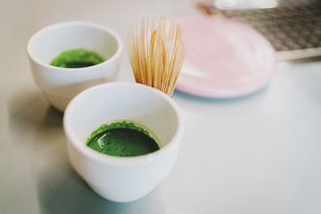 A set of two cups with a freshly made green matcha tea and a traditional bamboo whisk for whipping matcha powder. Tea making ceremony in an asian coffee shop. Healthy and tasty beverage.