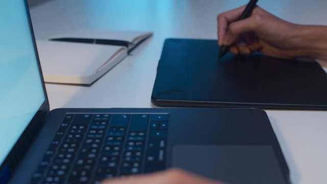 Cheerful young graphic designer lady using digital graphic tablet while working late in modern office at night, Asia professional female using laptop computer retoucher sitting in living room at home.
