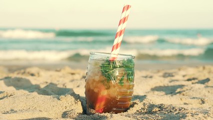 Misted glass of drink on sand on beach