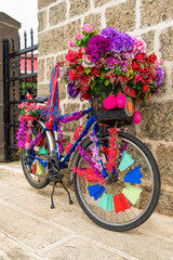 Real bicycle decorated with plastic and fabric flowers leaned stone wall
