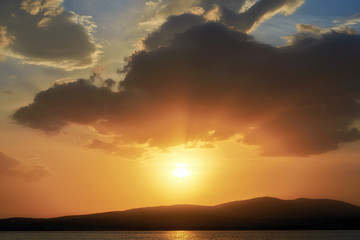 Fototapeta premium Landscape with a dramatic fiery sunset on the Black Sea coast. The rays of the sun make their way through the clouds