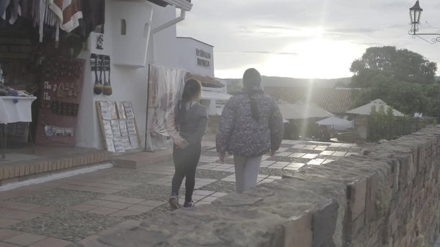 Slow-mo of two girls walking on colonial style plaza at sunset time
