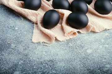 Black Easter eggs on a linen napkin on a blue texture table. Easter celebration concept. Copy space