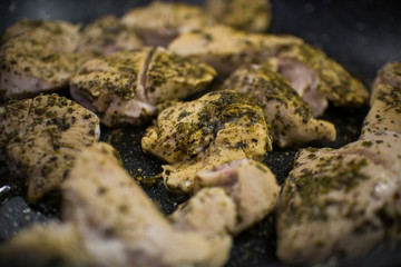 Slices of fried chicken sprinkled with herbs in a dark kitchen pan close-up.