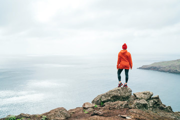 Trail runner female dressed orange sporty hoodie and red cap resting on the cliff and enjoying...