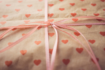 Gift in paper packaging with a pattern of red hearts with ribbon bow.