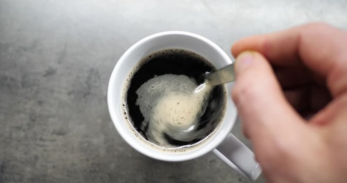 Male Hand Cup Of Hot Coffee Closeup Top View. Business And Drink Concepts. Top View Of Person Hand Stirring Coffee With Spoon On Gray Wooden Table. Close Up