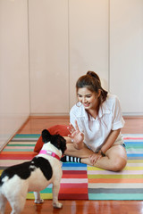 beautiful young asian woman wearing white shirt and holding red pillow who sitting and playing with her cute dog with happy and smiling face in living room. (lifestyle concept)