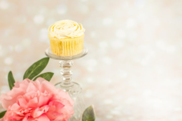 Cupcake on a crystal pedestal with flowers peony on a bokeh cream sweet glitter sparkle background