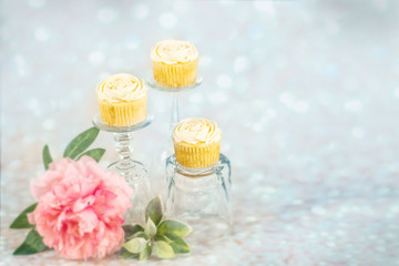 Three vanilla flower decorative cupcakes on crystal pedestals with blue glitter sparkle background in multiple colors