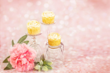 Three vanilla flower decorative cupcakes on crystal pedestals with pink glitter sparkle background in multiple colors