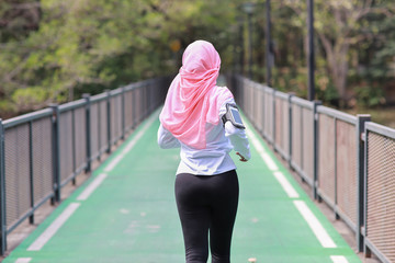Rear view portrait sporty young asian muslim woman in sportswear jogging outdoor for marathon training. Jogger girl exercising along concrete path outdoor with green tree background. Sport concept