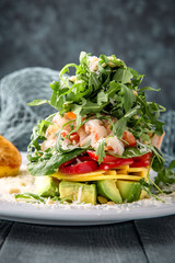 Sea salad of shrimp, avocado, tomato and cheese under arugula. On a turquoise background. Sea mood concept menu.