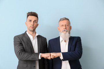 Portrait of senior man and his adult son bumping fists on color background
