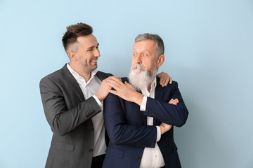 Portrait of senior man and his adult son on color background