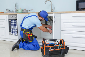 Plumber repairing sink in kitchen