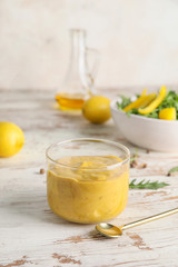 Glass of tasty honey mustard sauce on white wooden table