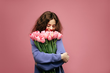 Flowers smell. Young girl holding bouquet of pink tulips flower against pink background