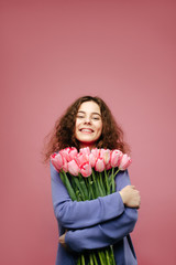 Girl holding bouquet of spring flower tulips against pink background. International womans day