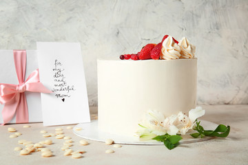 Tasty cake with greeting card and gift for mother on grey background