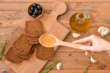 Woman pouring tasty olive oil from spoon on fresh bread