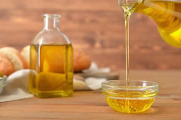 Pouring of tasty olive oil from bottle into bowl on table