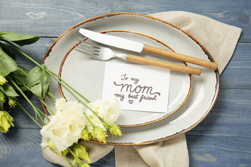 Table setting with card for Mother's day dinner on color wooden background