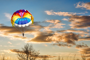 A man is gliding with a parachute on the background of sunset.
