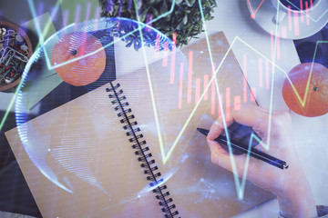 Forex chart hologram on hand taking notes background. Concept of analysis. Double exposure