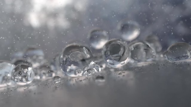 Fluid Bubbles Bounce on Water Resistant Surface with Rain Drops Falling Around.