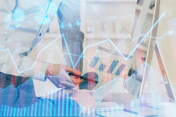 Double exposure of chart with businessman typing on computer in office on background. Concept of hard work.