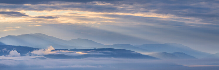 Dawn in a mountain valley, morning fog and clouds, panoramic view