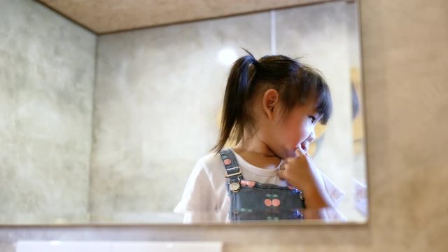 Cute little child girl doing makeup and having fun at a mirror in room.