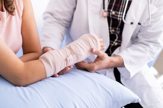 Bone specialist doctor examining serious injured woman at her arm with splint and bandage. Physician doctor talking to broken arm woman patient in the hospital. Healing in injured person concept.