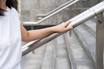 Woman walking on the stair way and grabbing on safety stair rail. Close up shoot on a hand catching a stair rail. Woman aware about safety while walking on the stair way.