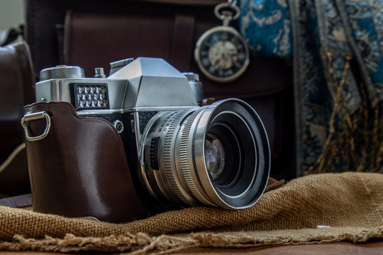 A vintage photo camera and A Brown leather bag with Scarf and Pocket watch on Sack cloth background.