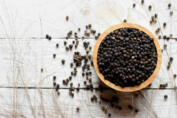 Black pepper seeds in a cup placed on a white wooden table.