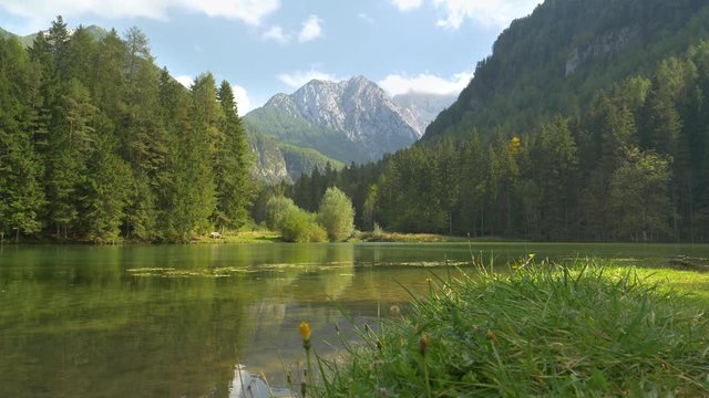 LOW ANGLE: Spectacular view of a rocky mountain in the Slovenian countryside overlooking the spruce forest and tranquil lake. Picturesque view of the woods surrounding a pond under a majestic mountain