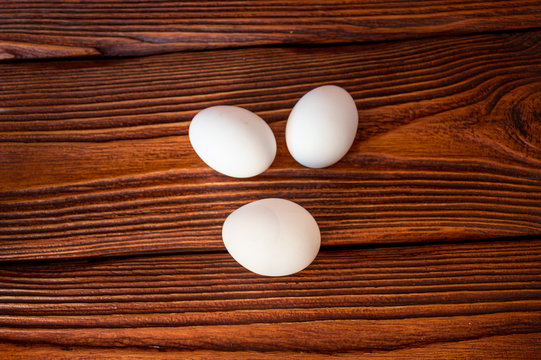 Three white chicken eggs on a wooden surface.