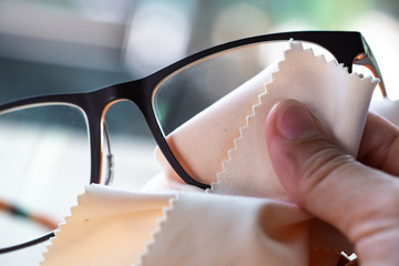Woman's right hand cleaning black eyeglasses by microfibre cleaning cloths, Close up & Macro shot,...