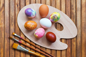 Beautiful multi-colored chicken Easter eggs on a cutting board in the form of a palette and brush next to it. Preparing for Easter. Still life, wooden background, flat lay, close-up