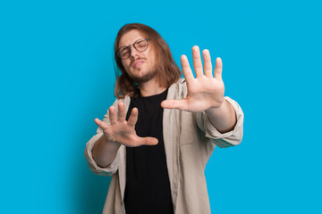 Caucasian man with long hair and beard is refusing something while posing on a blue background