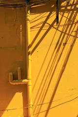 Close up grunge style yellow wall detail with pipes and shadows of concrete building exterior