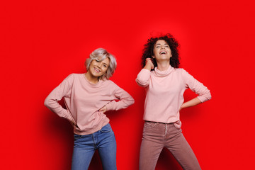 Curly haired caucasian lady is posing near her blonde friend with nice smile on a red background